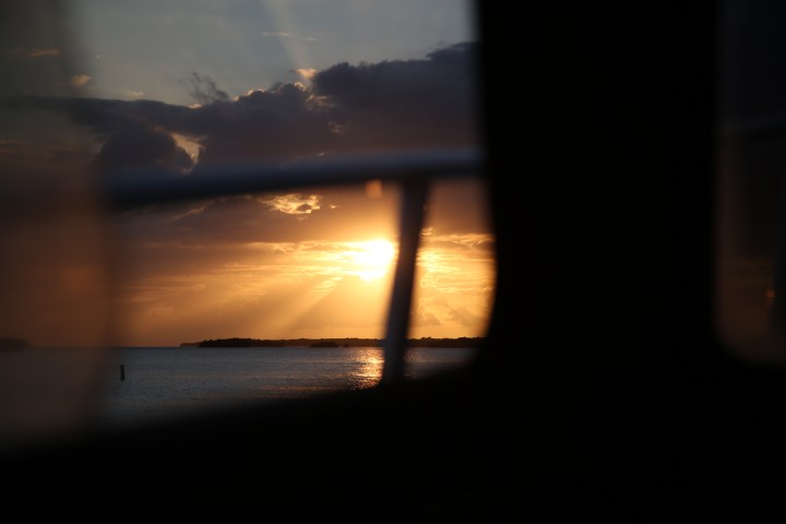Sunset over water with sun rays through clouds, framed by a window.