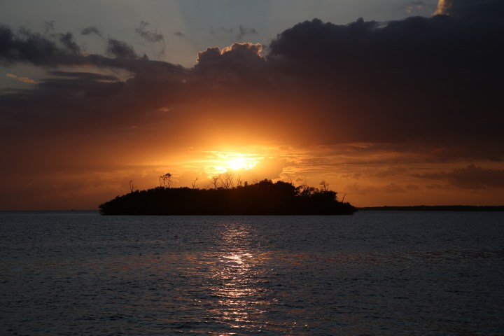 Sunset over the ocean with dark clouds and silhouetted island.