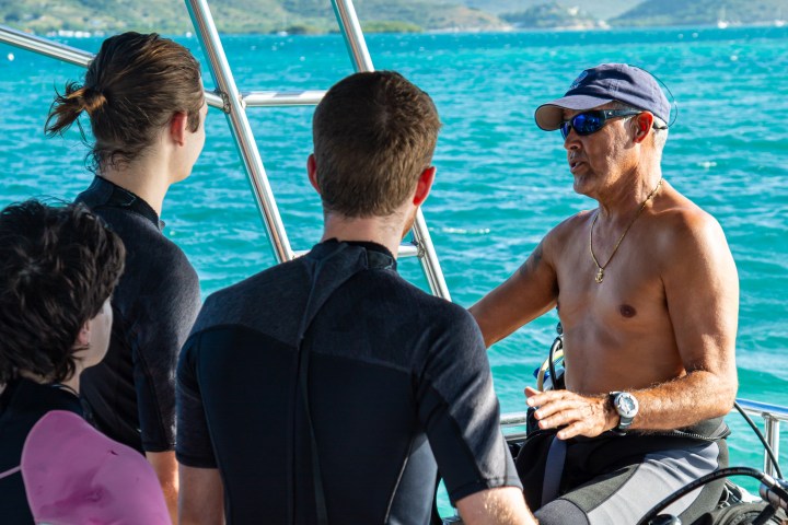 Instructor talking to three people on a boat, ocean and hills in the background.