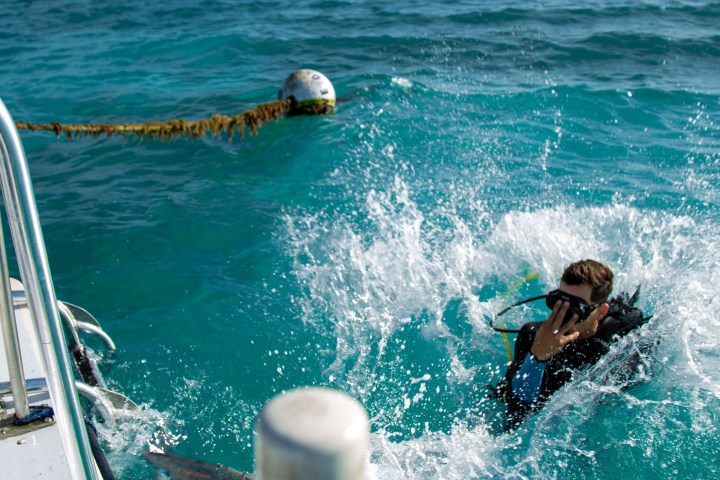 Scuba diver splashing into clear blue water from a boat.