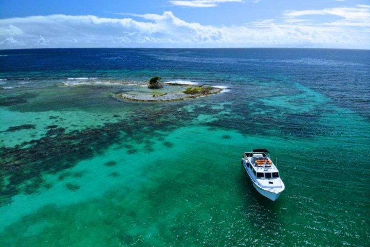 Aerial view of a boat near a small island surrounded by turquoise ocean waters.