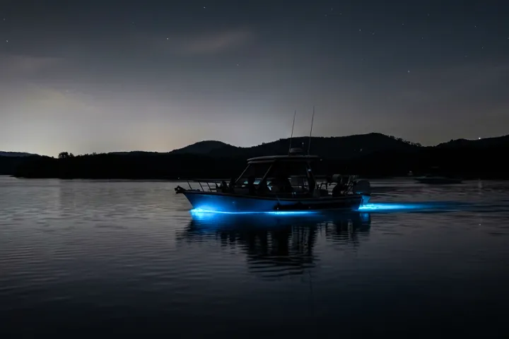 Boat with blue lights on water at night, surrounded by mountains.