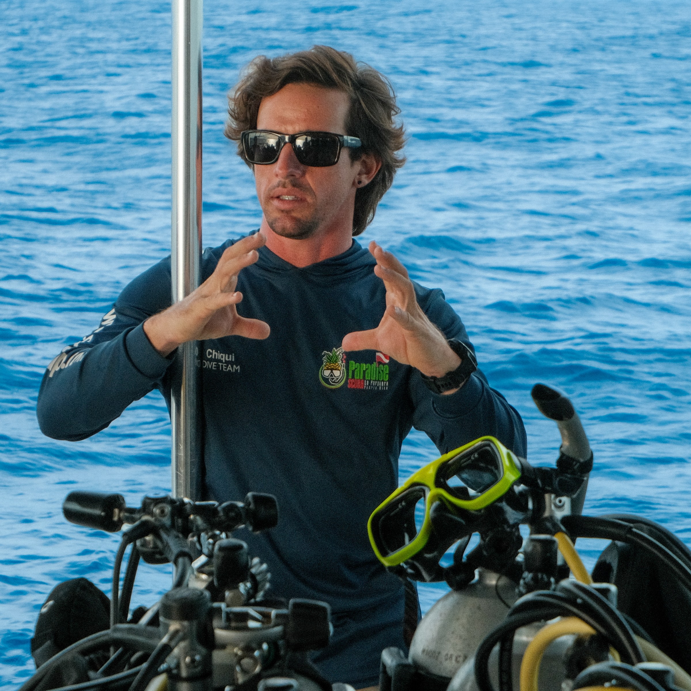 Person on a boat with scuba gear, gesturing while explaining.