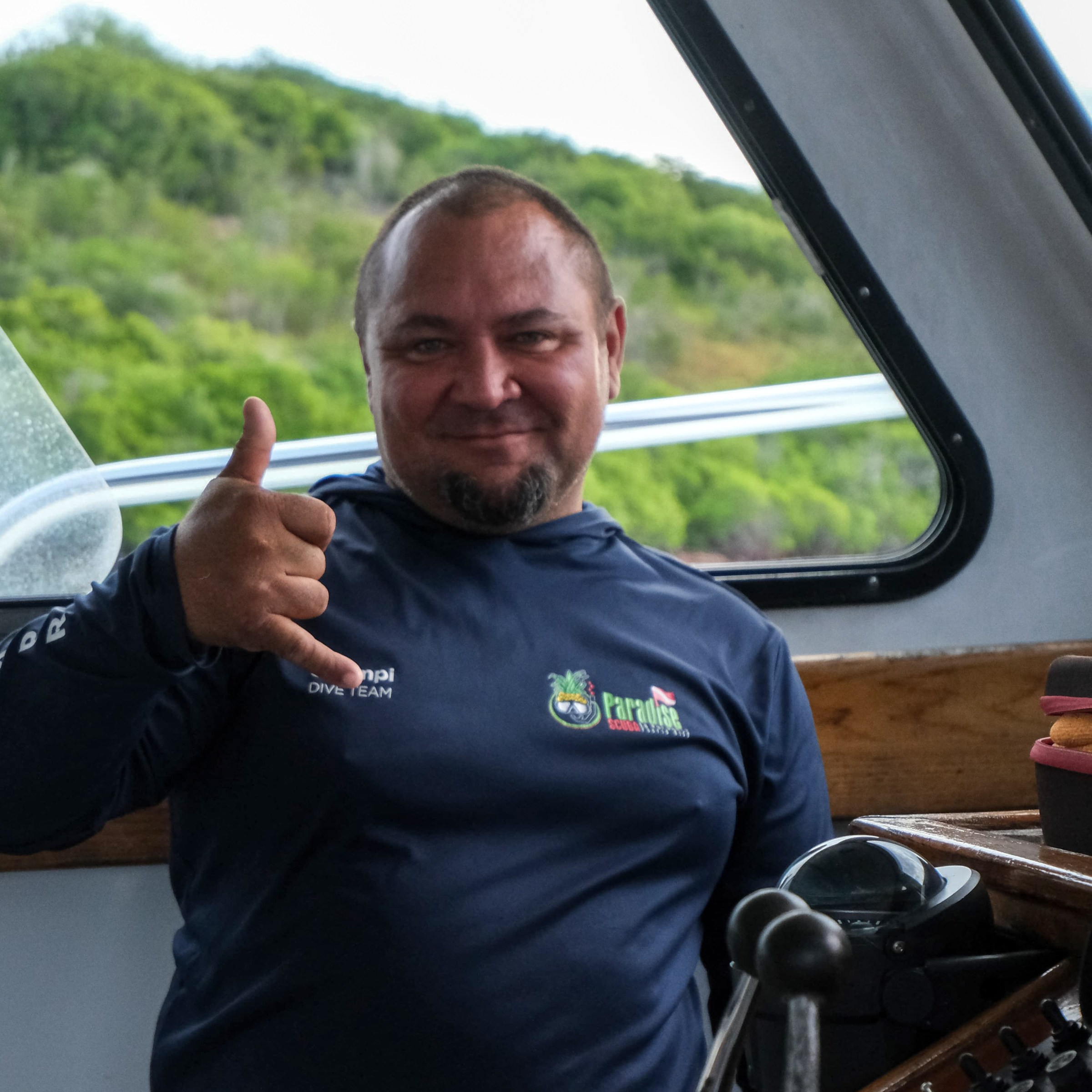 Man on a boat smiling and making a shaka sign with his hand.