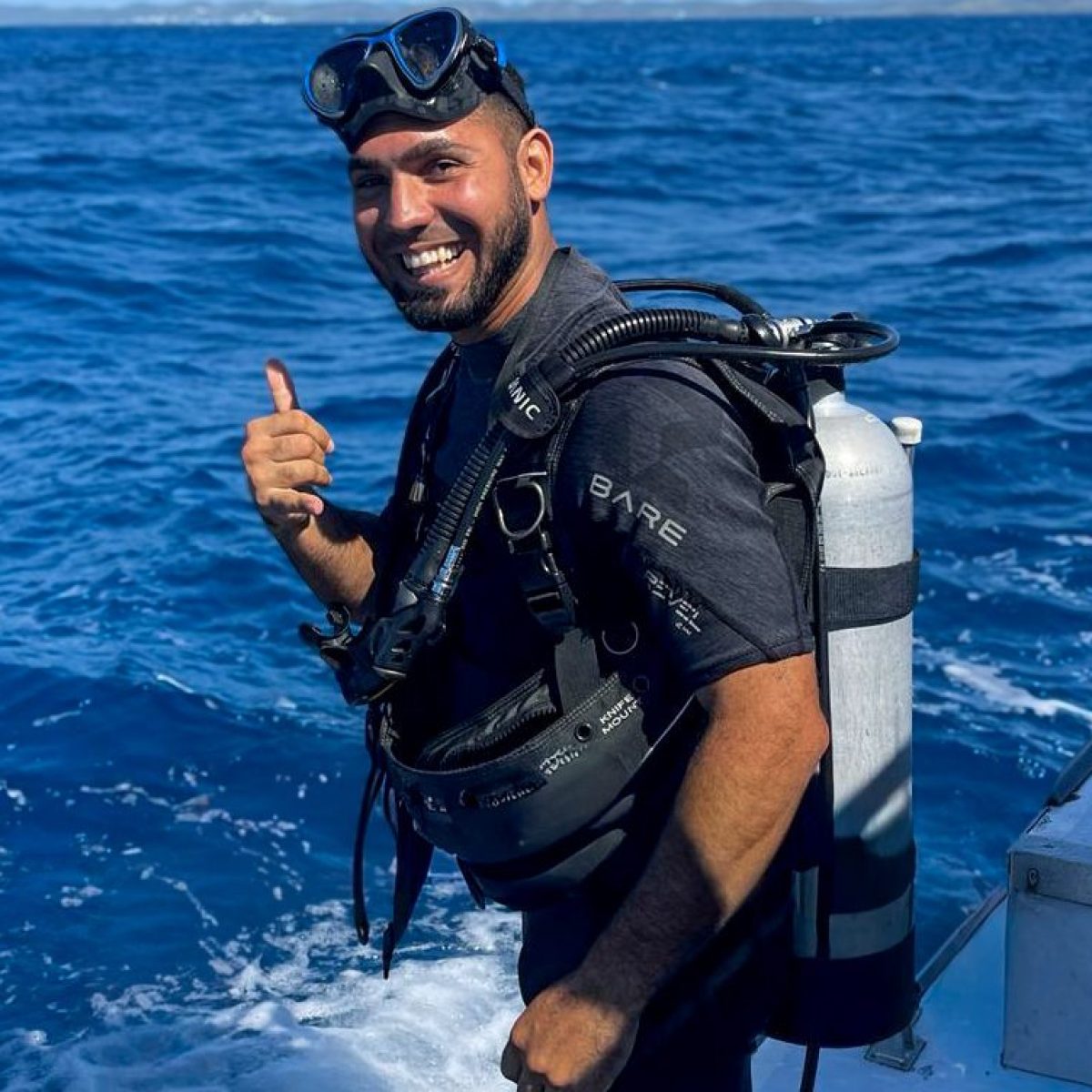Smiling diver with scuba gear giving thumbs up on a boat in the ocean.