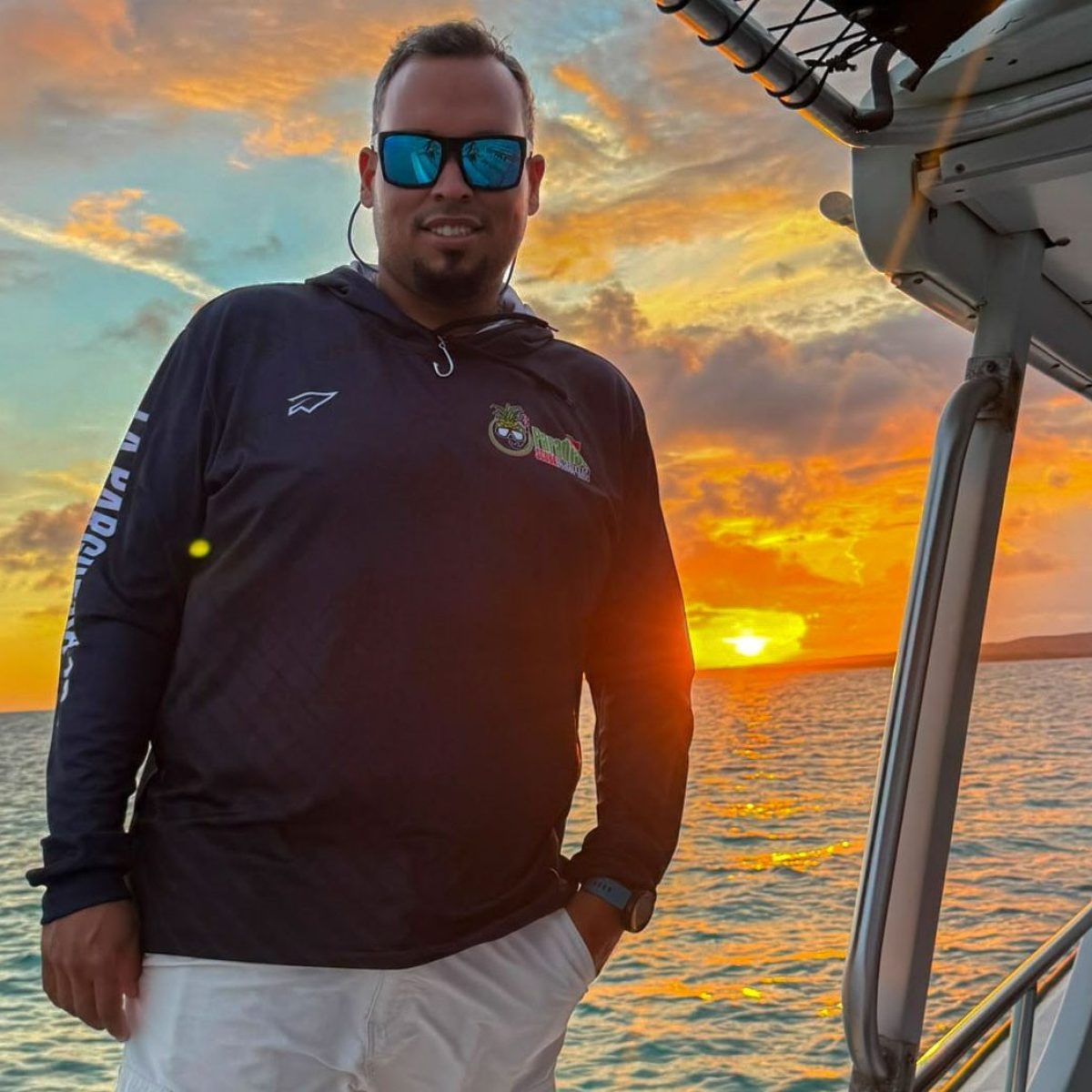 Person on boat at sunset, wearing sunglasses and dark jacket.