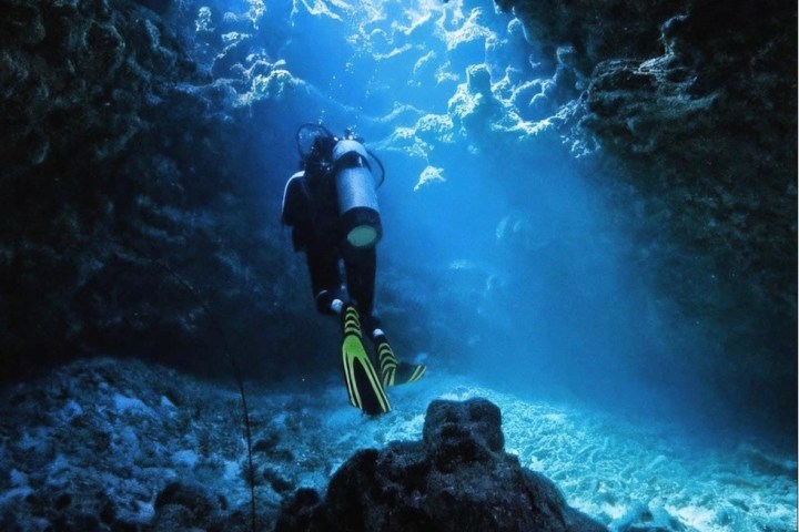 Diver swimming through an underwater cave surrounded by rock formations.