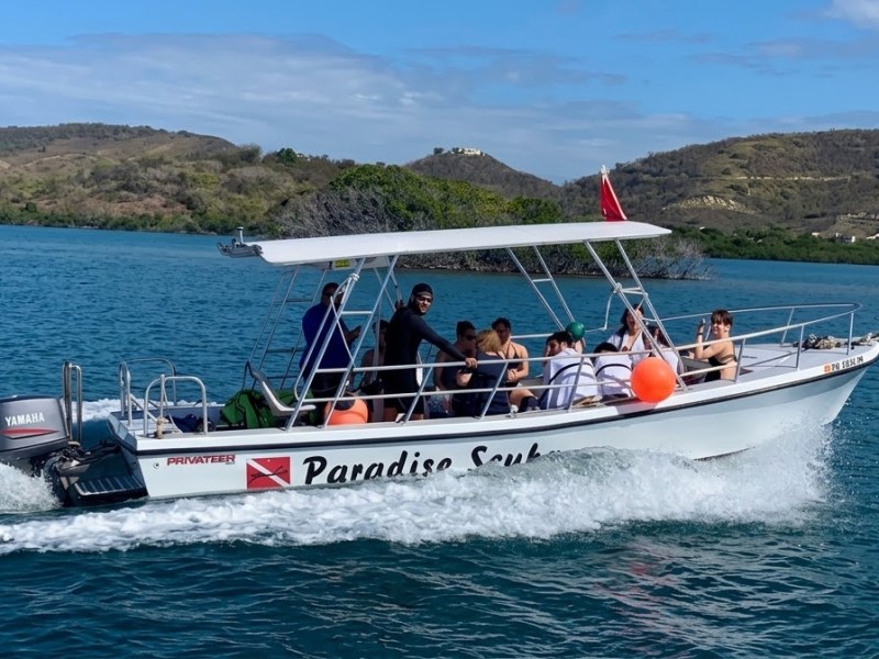 Small boat with passengers cruising on a lake with hills in the background.