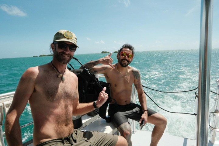 Two men smiling on a boat in sunny weather with ocean in the background.