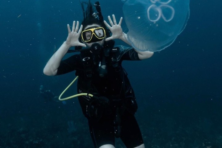 Scuba diver underwater with hands up near a jellyfish.